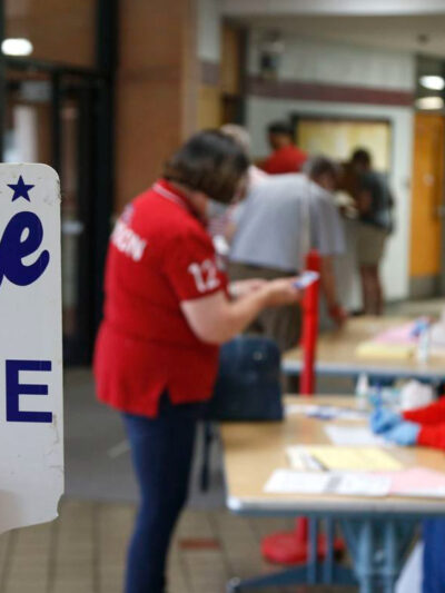 Photo of a polling place with two people and a sign that reads "vote here"
