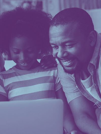 A picture of a black family smiling together as they stare at a computer, with a blue overlay on the photo.