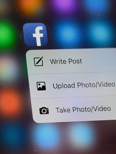 A hand holding a phone with a Facebook app on the screen.