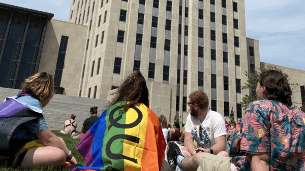 Image of people sitting on grass, one has a pride flag