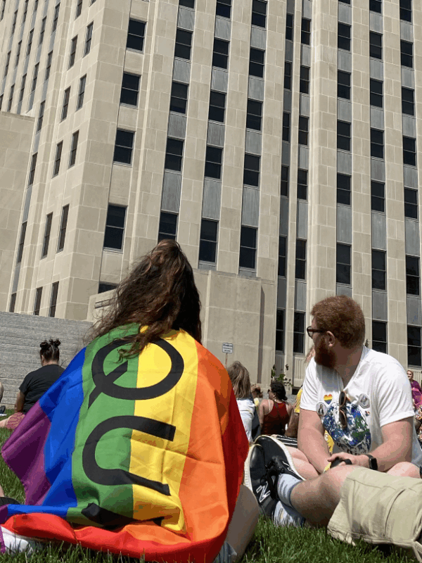 Image of people sitting on grass, one has a pride flag