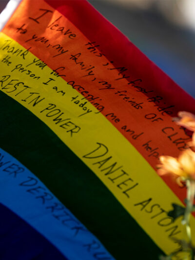 A waving rainbow flag reading "Rest In Power Daniel Aston" sits at the memorial created outside of Club Q.