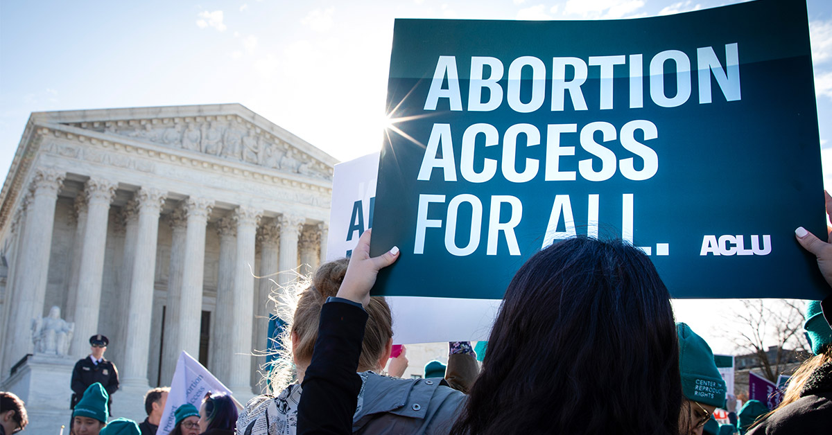 Person holding a sign that reads, “Abortion access for all.”