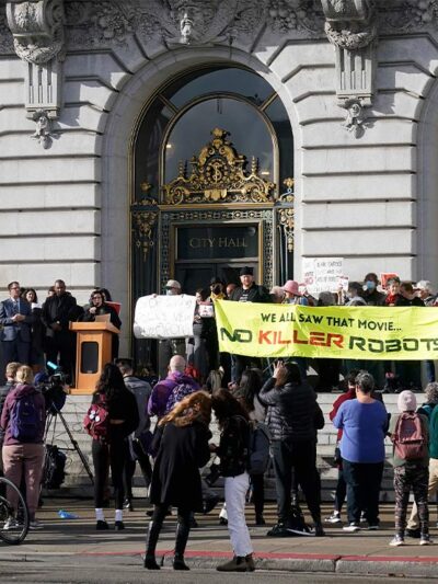 Demonstrators, (holding various signs, with the most prominent reading "WE ALL SAW THAT MOVIE ... NO KILLER ROBOTS") protest the use of robots by the San Francisco Police Department outside of City Hall in San Francisco, Monday, Dec. 5, 2022.