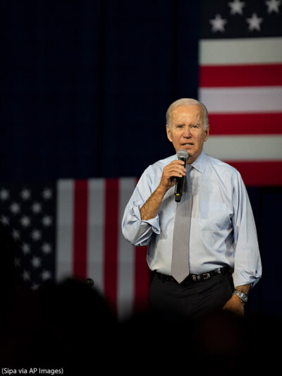 Joe Biden speaking in front of several American flags.