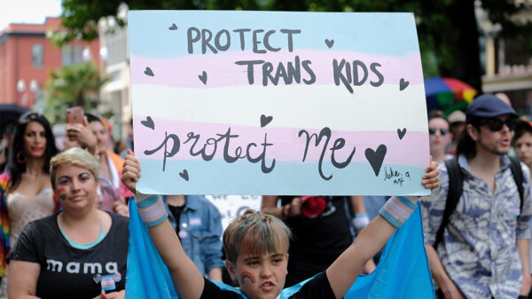A young child holds up a sign reading "PROTECT TRANS KIDS, PROTECT ME - luke, age 9" at a Trans Pride March.