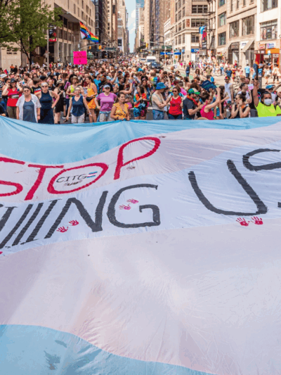 Trans flag with overlaying text that reads, “Stop killing us.”
