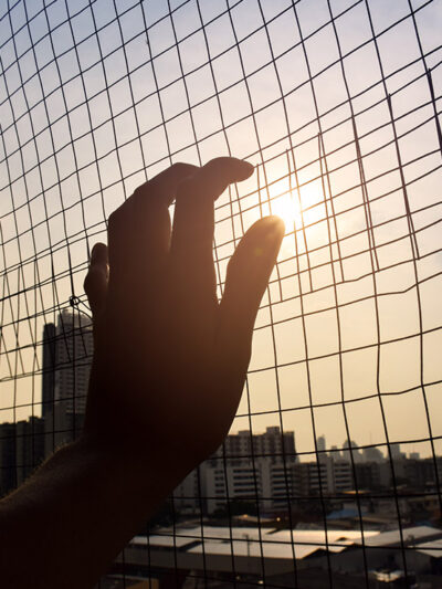 The silhouette of a hand holding on to a gate.
