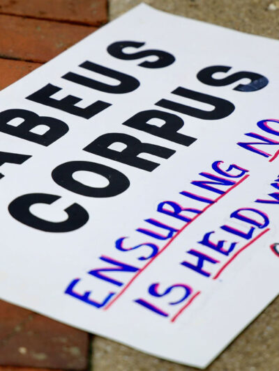 A sign reading " HABEAS CORPUS Ensuring No One is Held Without Charge" lying on the ground.