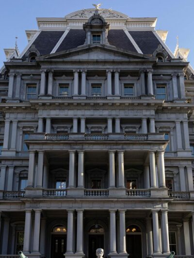 Front view of the Eisenhower Executive Office Building, which houses the U.S. Office of Management and Budget, showing the historic government building's rows of windows, ornate columns, and central staircase under a clear blue sky.