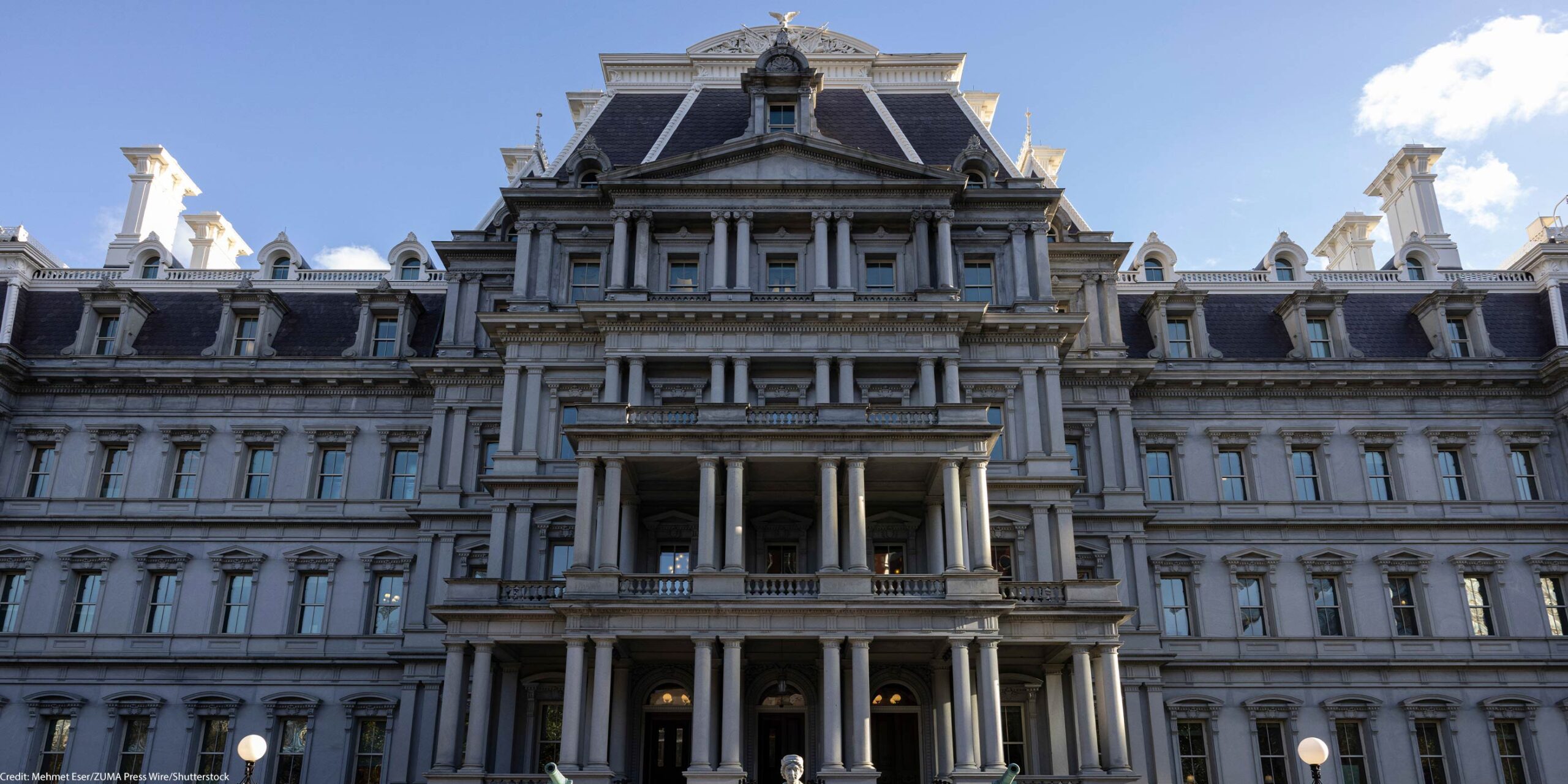 Front view of the Eisenhower Executive Office Building, which houses the U.S. Office of Management and Budget, showing the historic government building's rows of windows, ornate columns, and central staircase under a clear blue sky.