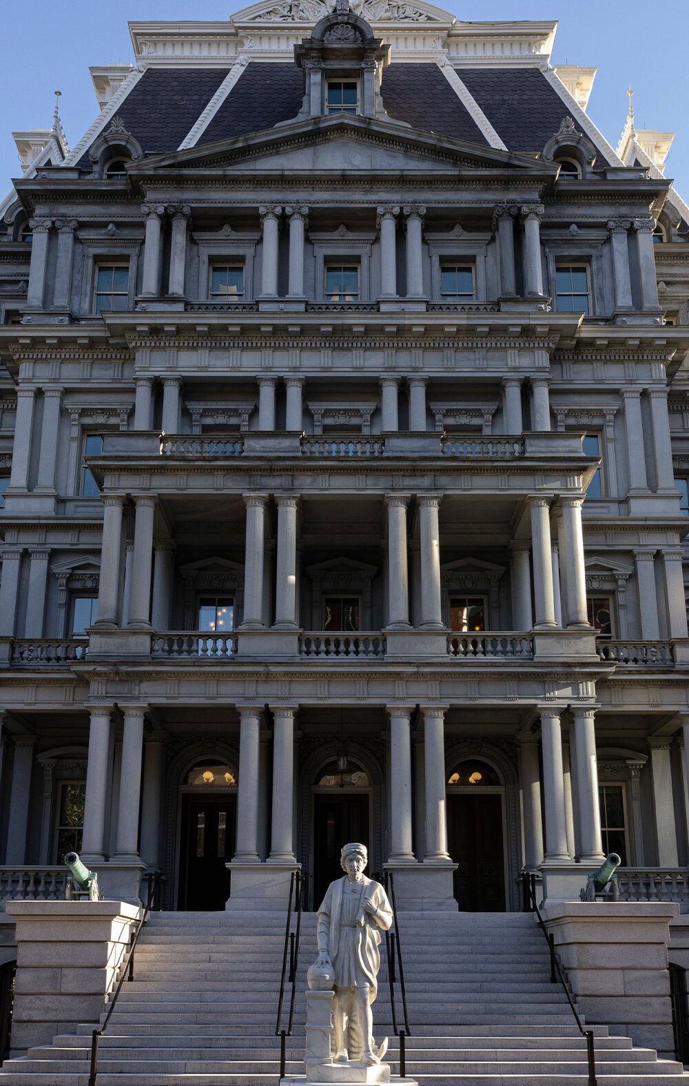 Front view of the Eisenhower Executive Office Building, which houses the U.S. Office of Management and Budget, showing the historic government building's rows of windows, ornate columns, and central staircase under a clear blue sky.