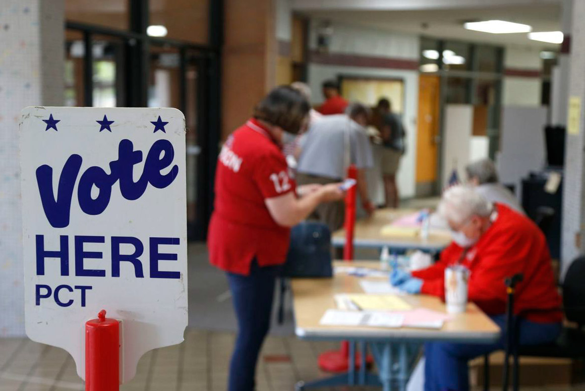 Photo of a polling place with two people and a sign that reads "vote here"