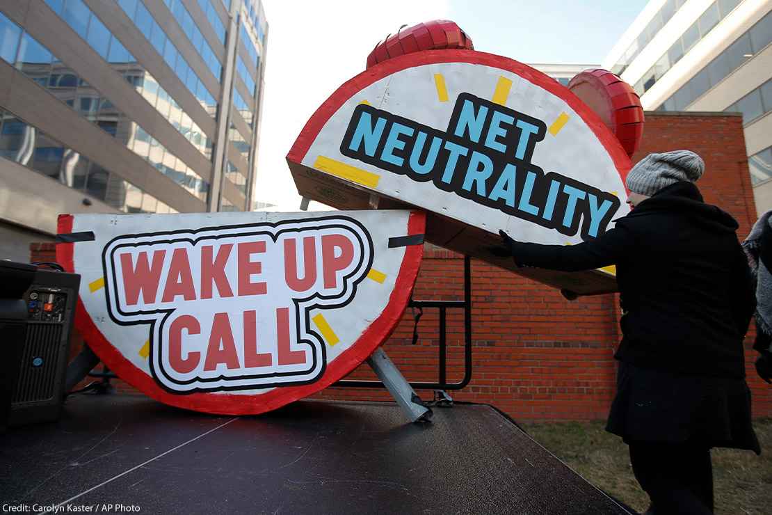 Woman helps to dismantle a large alarm clock display that reads "Net Neutrality Wake Up Call" from the stage after a protest in front of the FCC in Washington, DC.