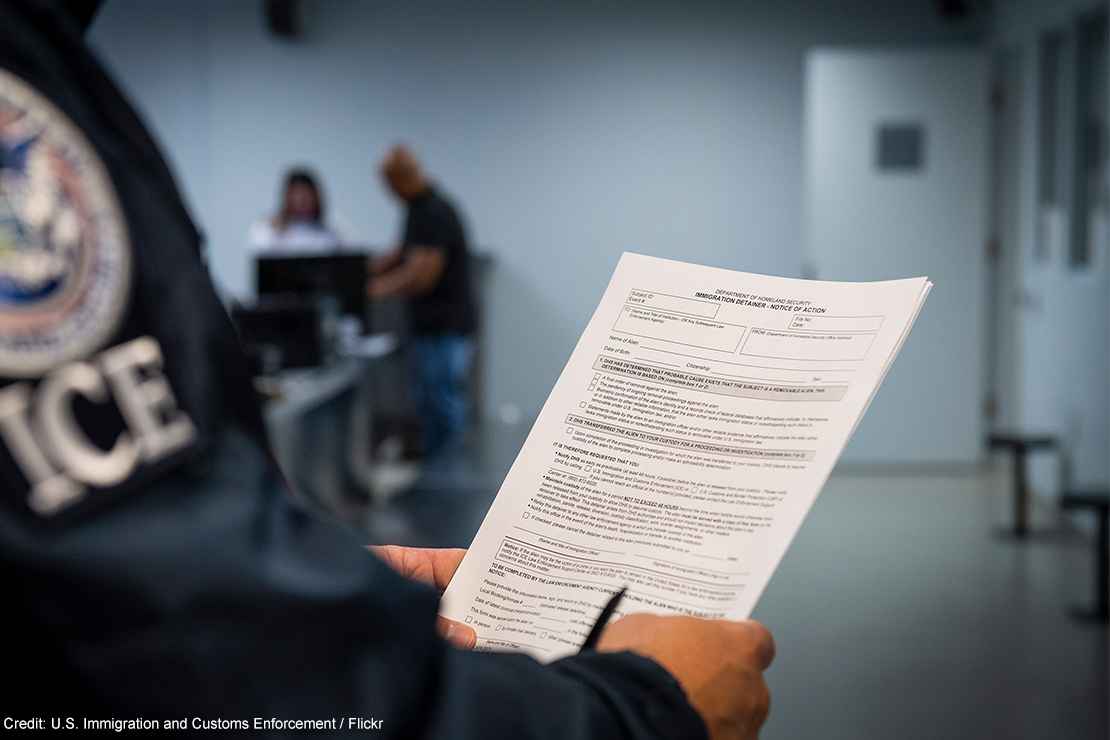 An ICE agent holding an Immigration Detainer form.