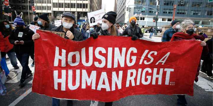 Protesters marching and holding a sign reading Housing Is A Human Right.