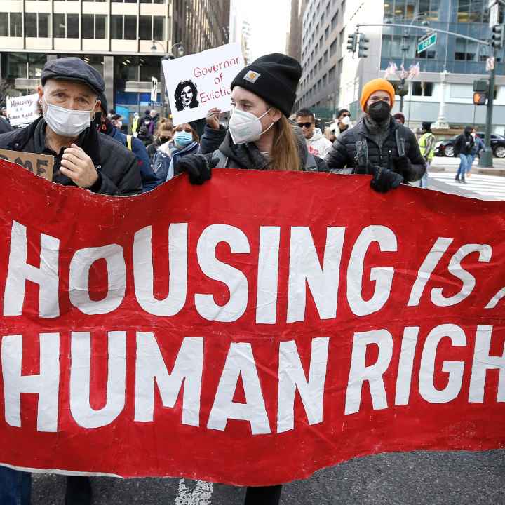Protesters marching and holding a sign reading Housing Is A Human Right.